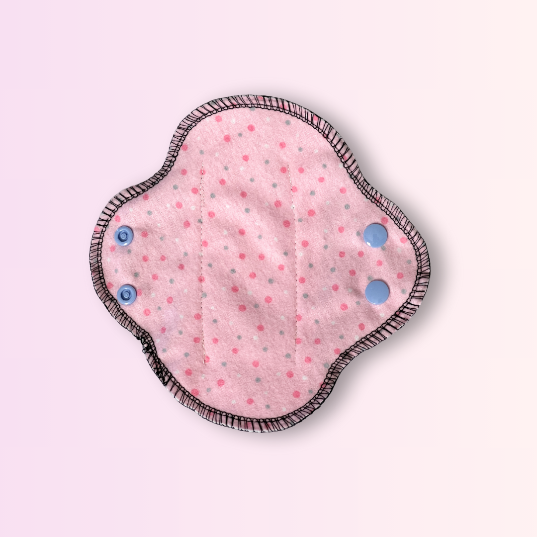 Reusable day pad with pink polka dot pattern and black wings open – eco-friendly cloth pad for light to heavy flow.
