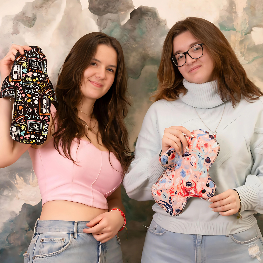 Two young women holding colorful reusable cloth menstrual pads, representing the next generation of Hume’s Period Care