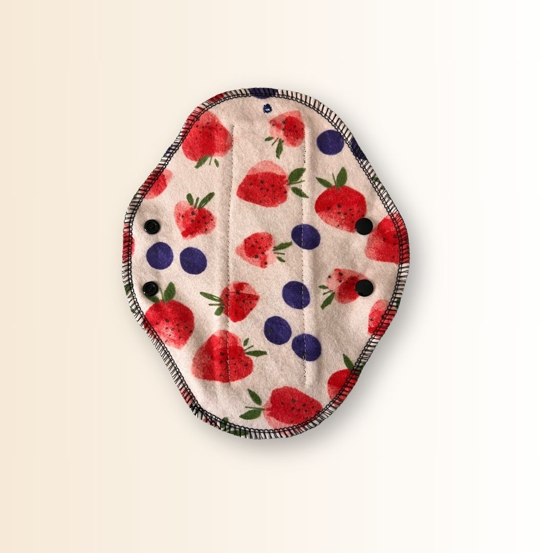 Reusable day pad with strawberry and blueberry print, shown with black wings open