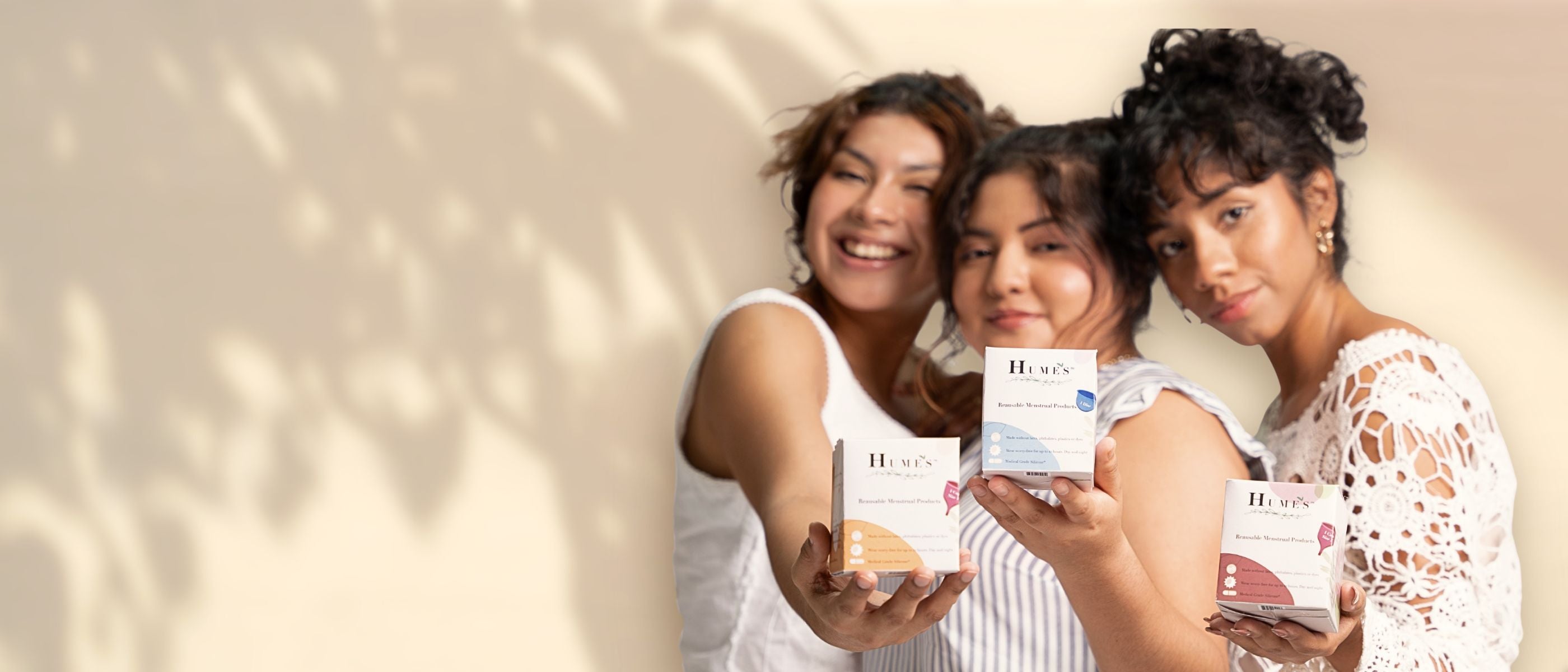Three young women holding Hume’s reusable menstrual cup boxes, promoting sustainable and eco-friendly period care