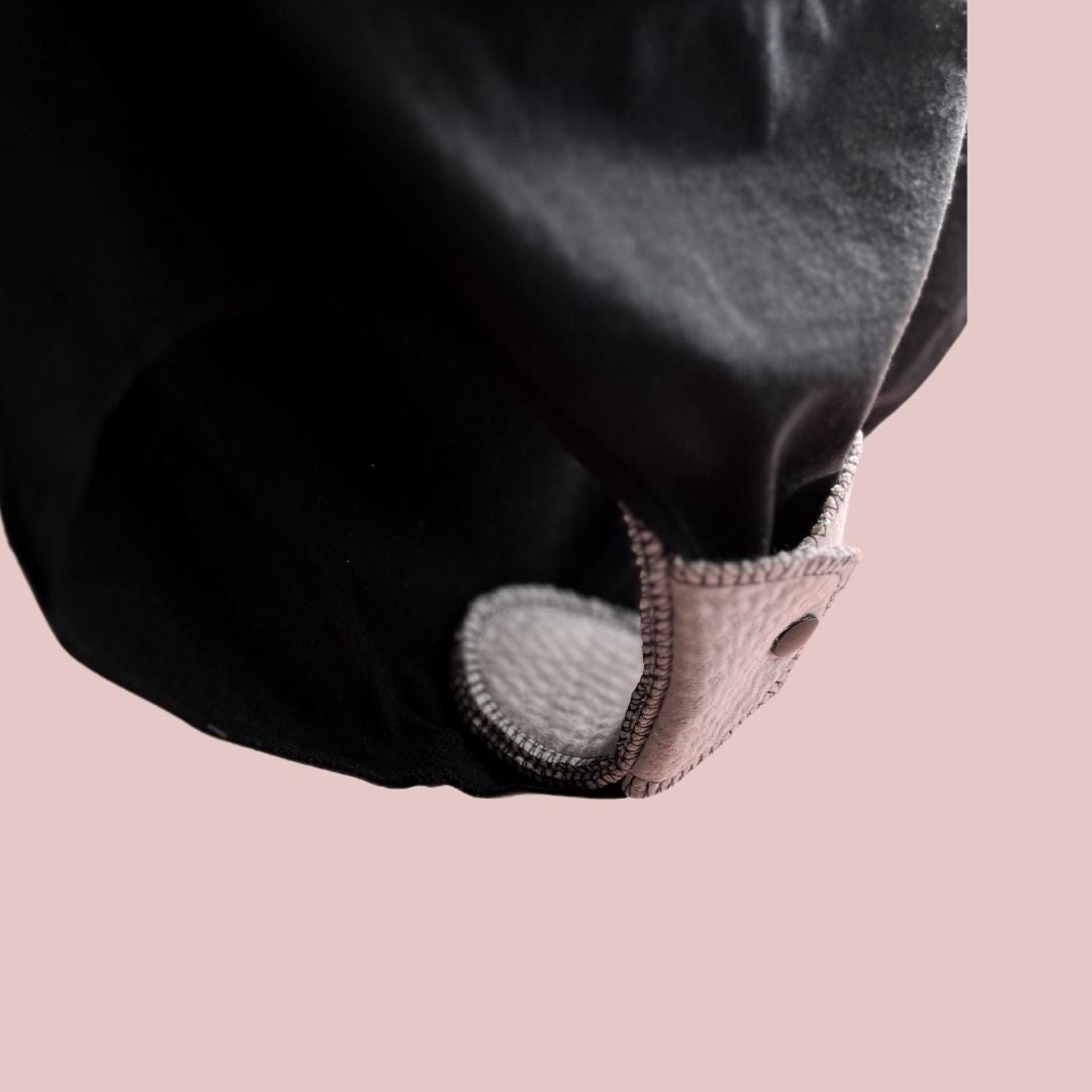 Organic cotton menstrual pad snapped onto dark underwear, close-up of secure fit