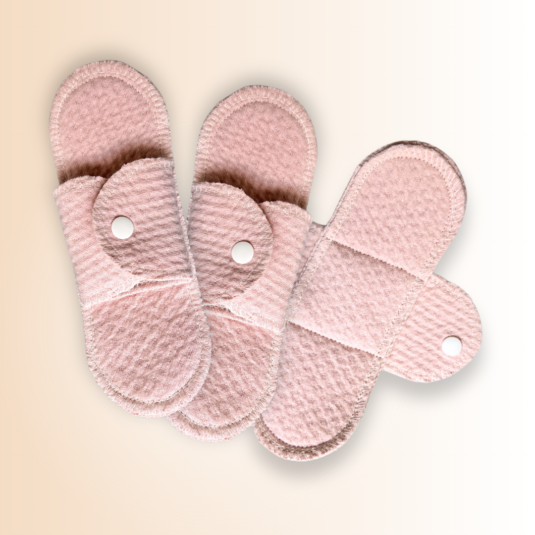 Three organic cotton cloth menstrual pads shown in open and closed positions on beige background