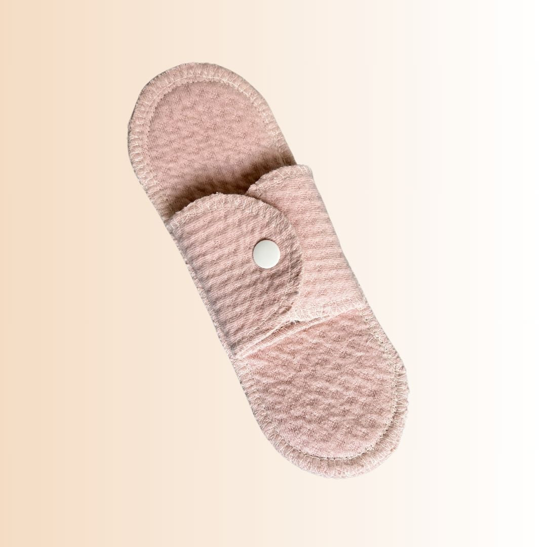 Single organic cotton reusable menstrual pad laid flat on soft gradient background