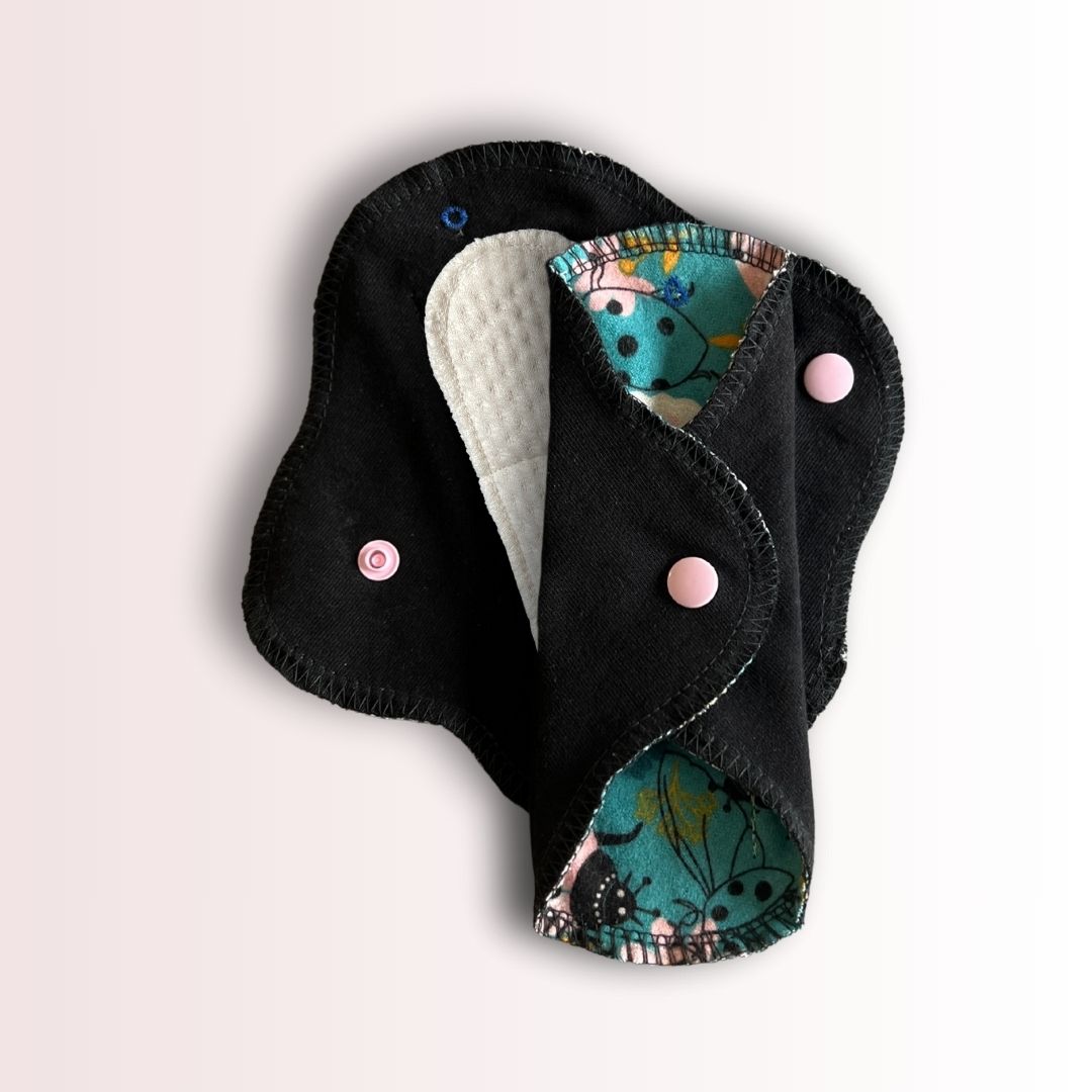Reusable teen cloth pad folded with visible absorbent organic cotton core and pink snap buttons
