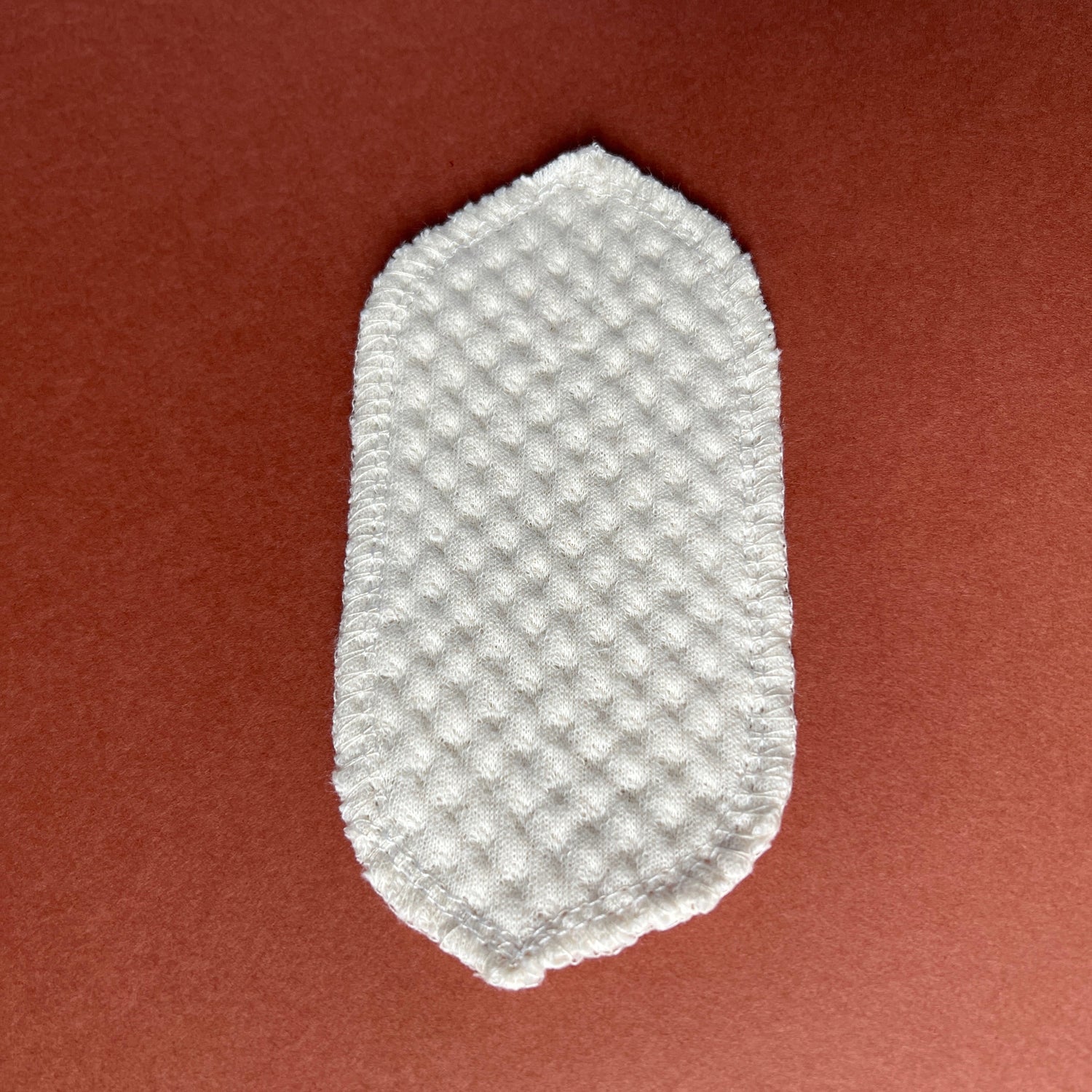 Reusable organic interlabial pad with a 100% organic cotton core, displayed on a brown and orange background