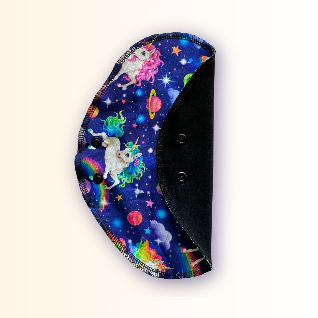 Folded unicorn reusable period pad showing rainbow galaxy print, black cotton absorbent side, and snap wings from Hume’s Period Care.