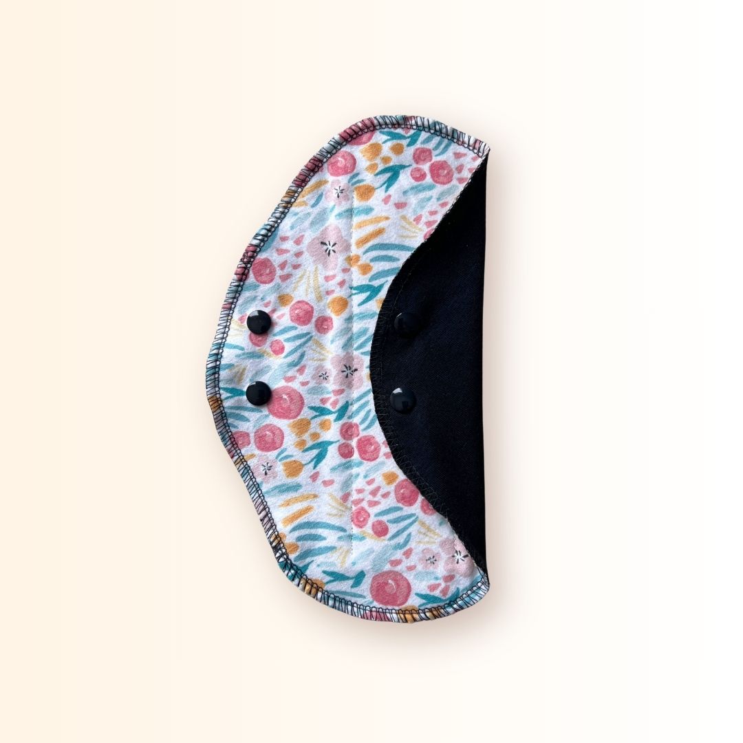 Floral reusable cloth pad folded and snapped for compact storage in a bag or wrapper.