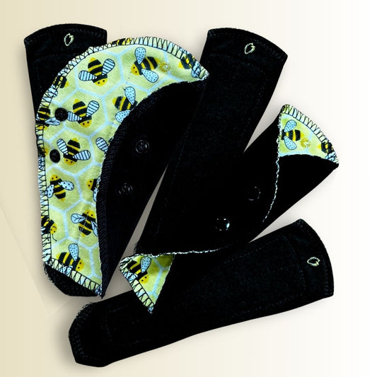 Five reusable thong panty liners with yellow bee print fabric arranged in a fan shape