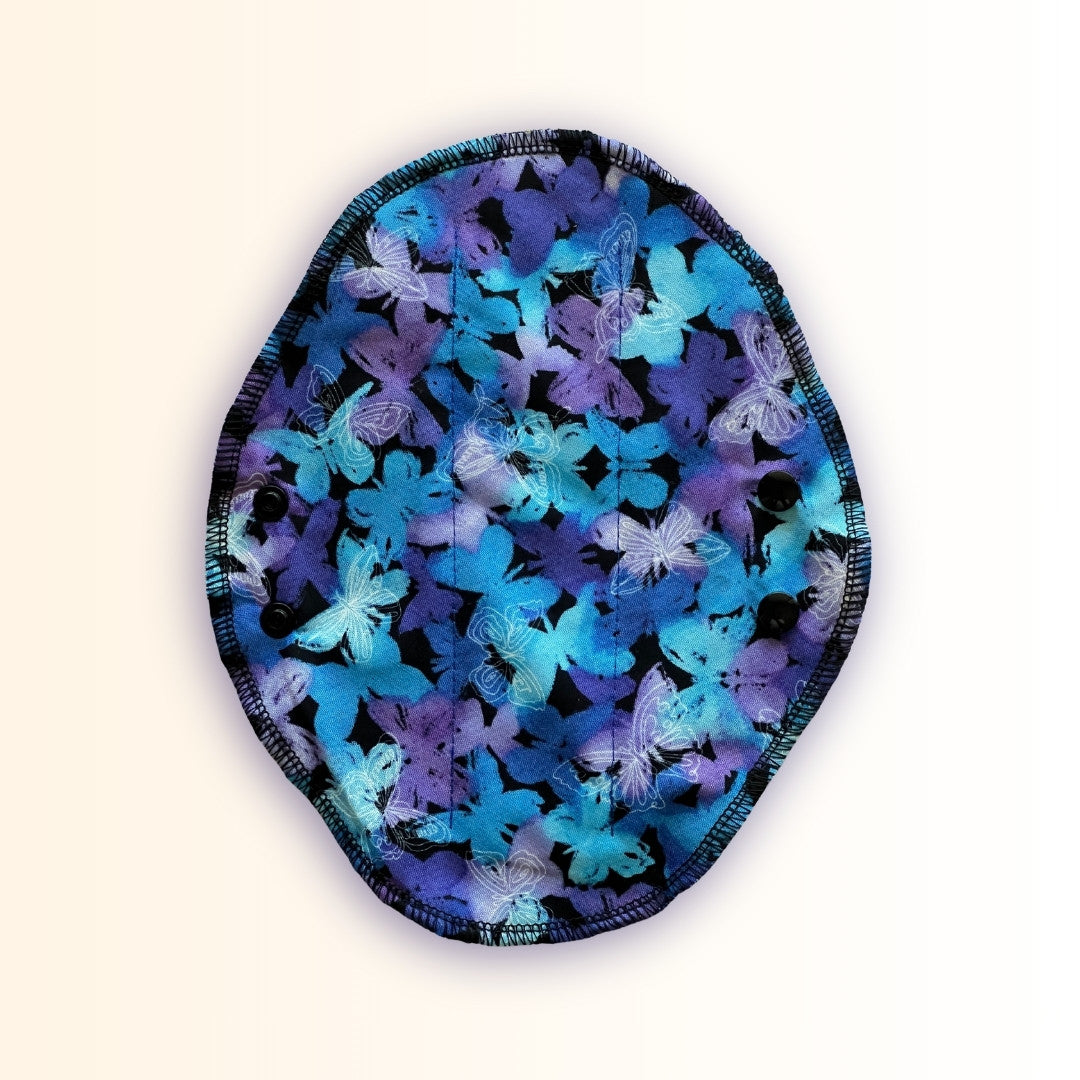 Blue butterfly reusable period pad shown open with blue and purple butterfly print, black snaps, and washable cloth design from Hume’s Period Care.
