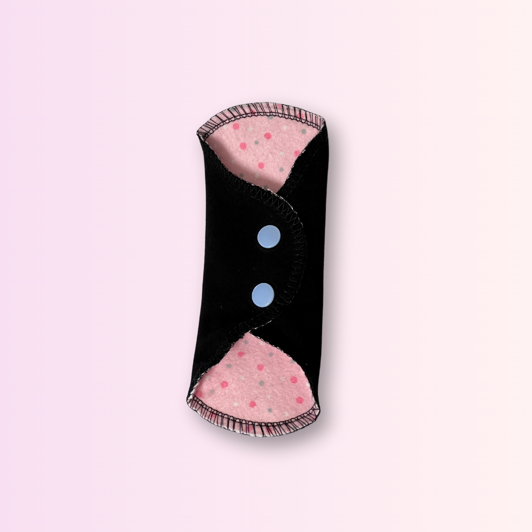 Cloth day pad in pink polka dot print with black wings snapped closed – washable, breathable, and sustainable.