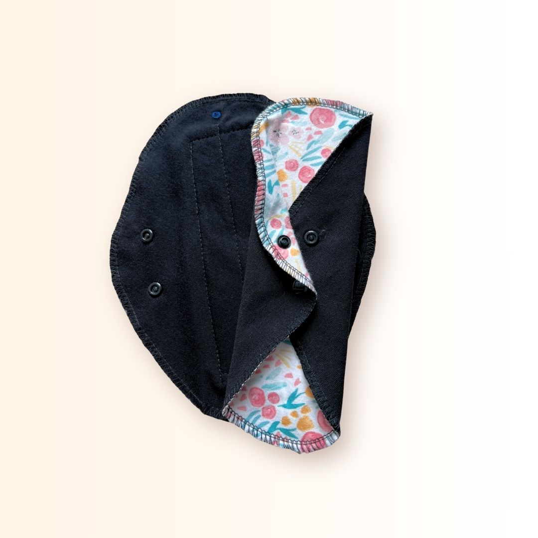 Floral reusable cloth pad folded and snapped for compact storage in a bag or wrapper.