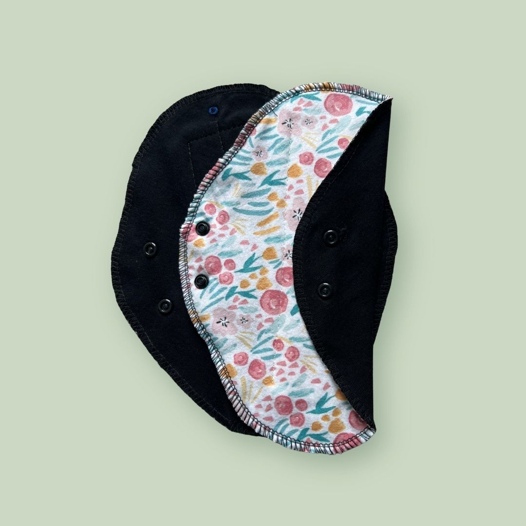 Floral print reusable cloth pad with black absorbent fabric and snap wings.