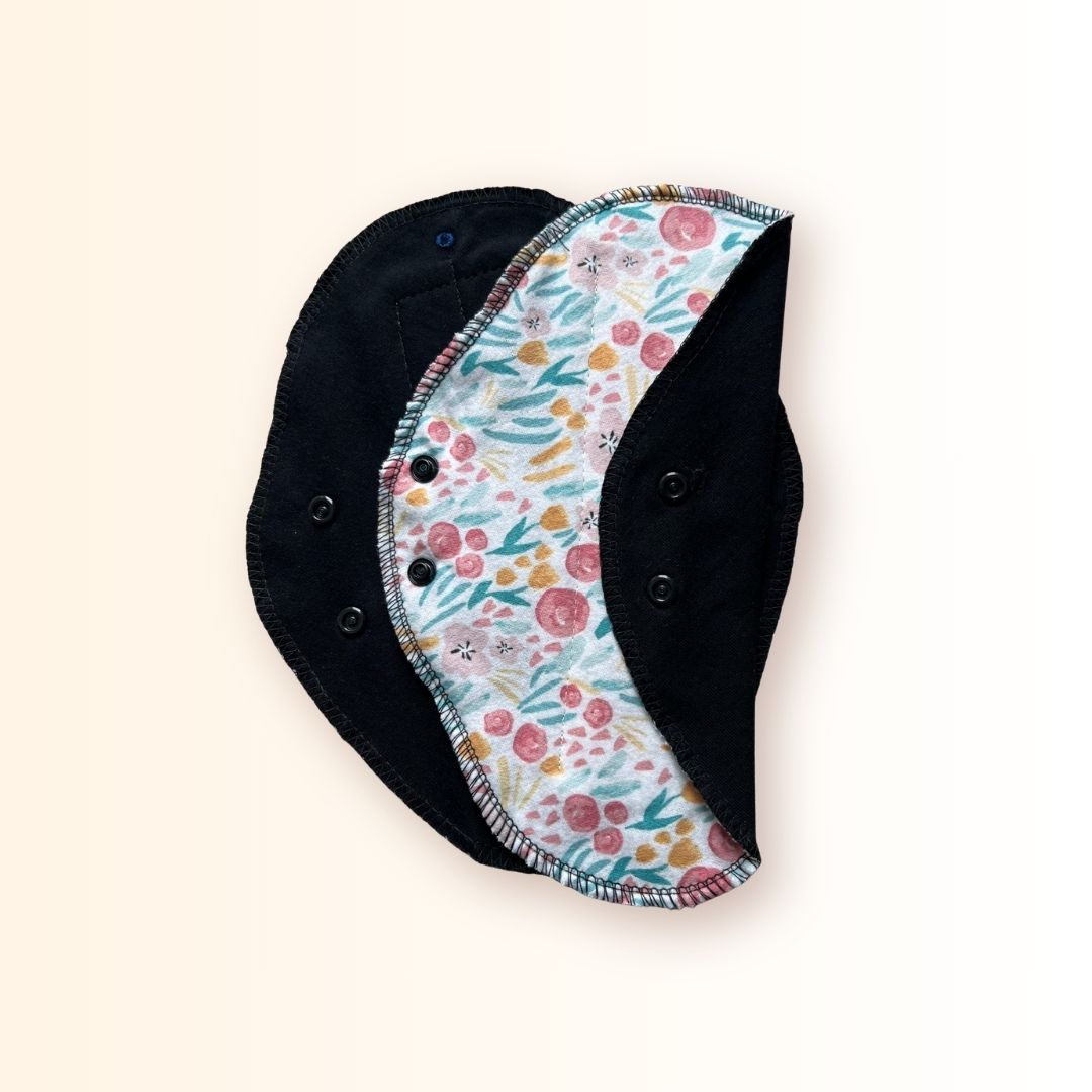 Floral reusable cloth day pad shown with its soft black absorbent side and snap wings.