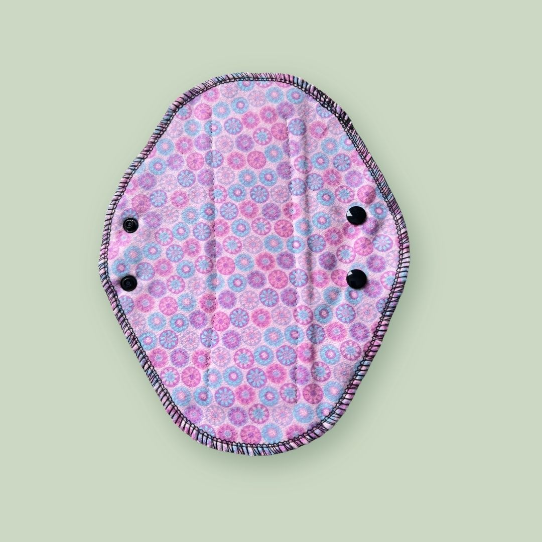 Pink patterned side of a reusable cloth period pad with adjustable snaps.