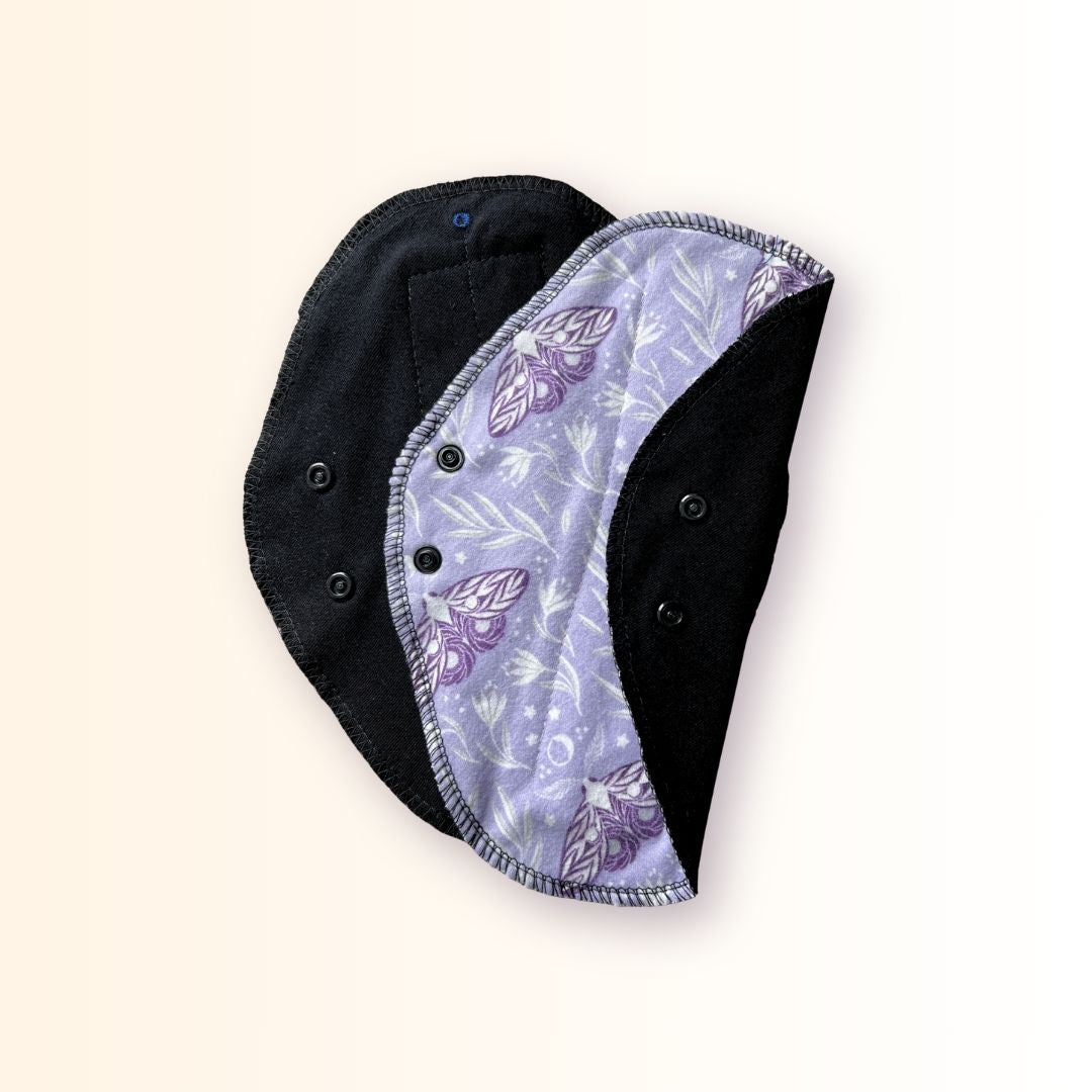 Lavender moth reusable day pad shown open beside a folded pad with black absorbent fabric.