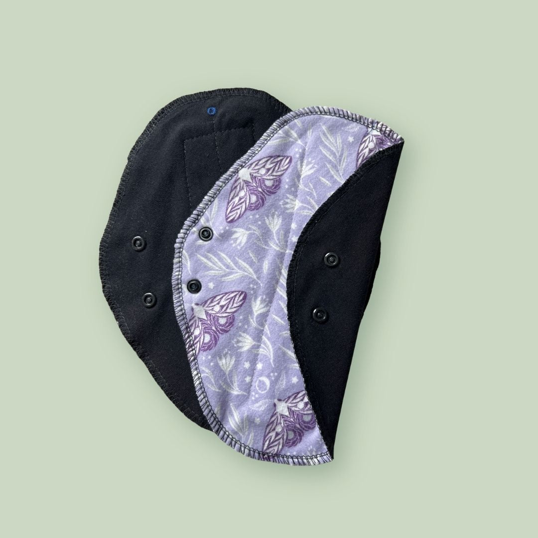 Lavender print reusable cloth pad with black absorbent fabric and snap wings.