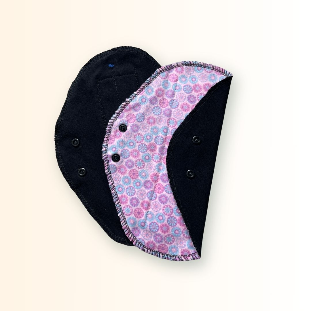 Pink mosaic reusable cloth day pad shown beside its soft black absorbent side with snap wings.