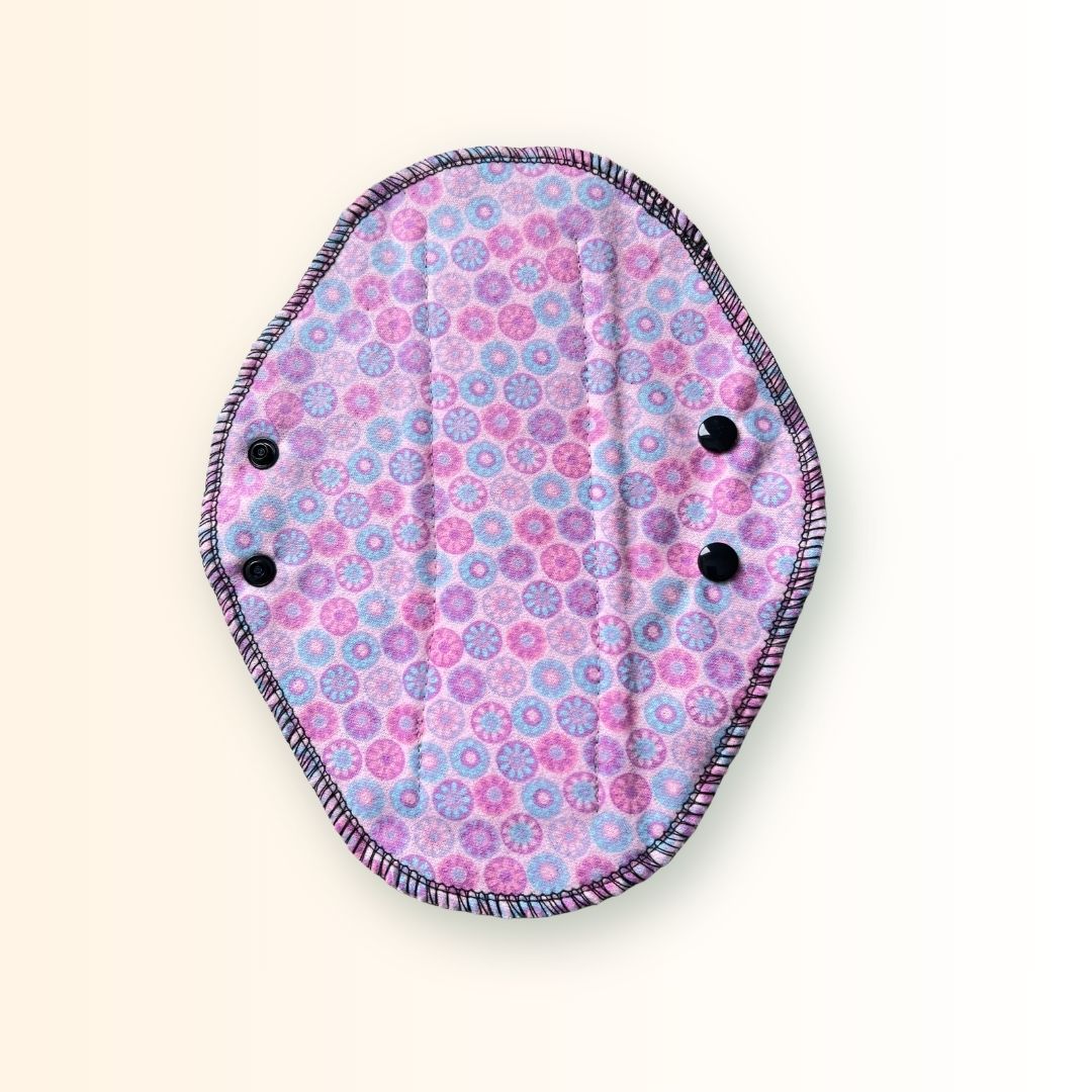 Full pink mosaic print side of a reusable cloth day pad with adjustable black snap wings.