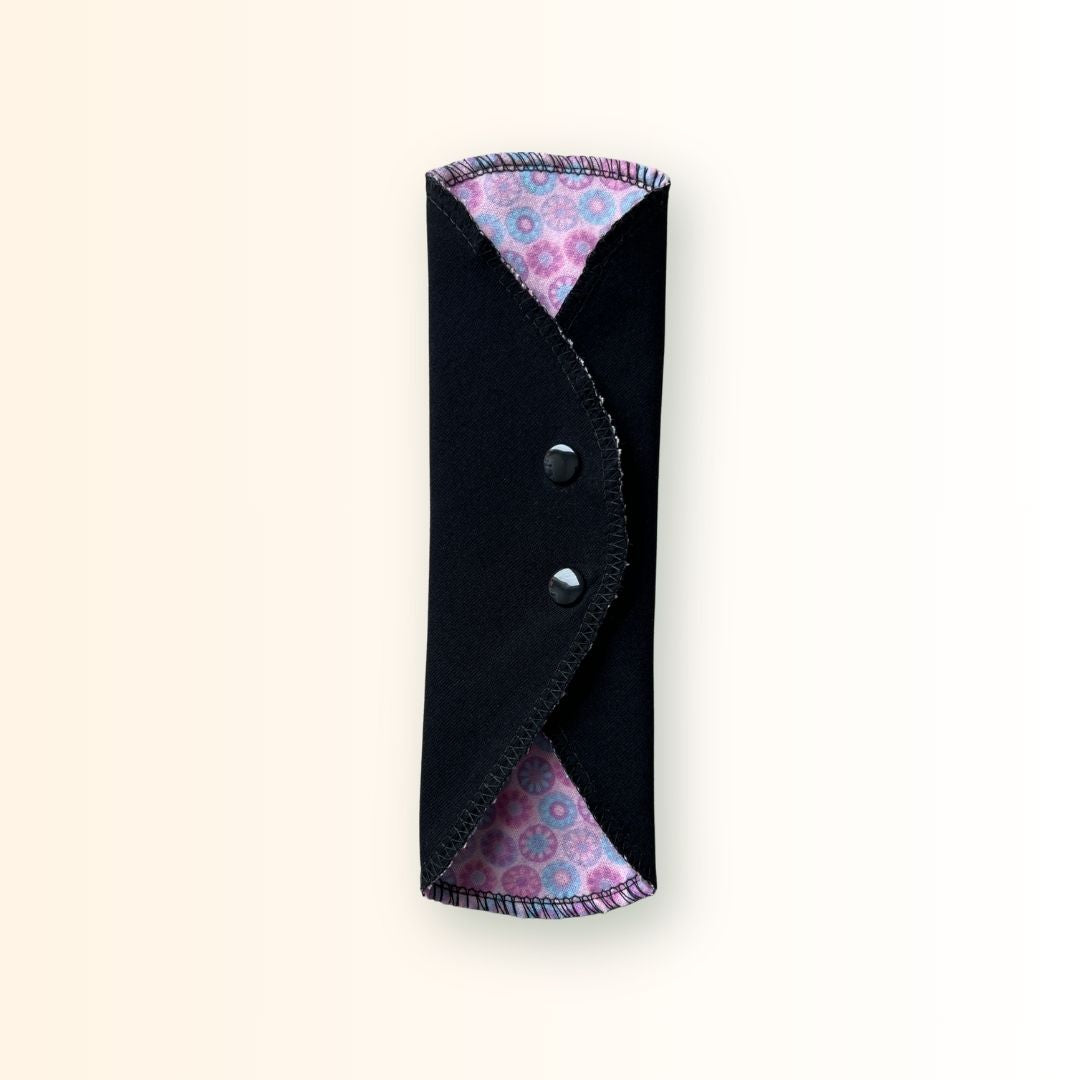 Pink mosaic reusable cloth pad folded and snapped for compact storage in a bag or travel wrapper.