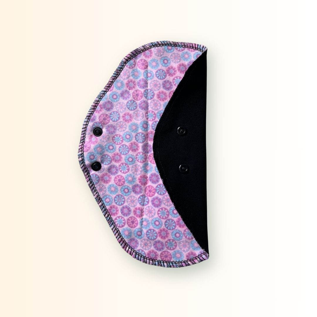 Pink mosaic reusable cloth pad partially folded to show its black absorbent side and snap closure.