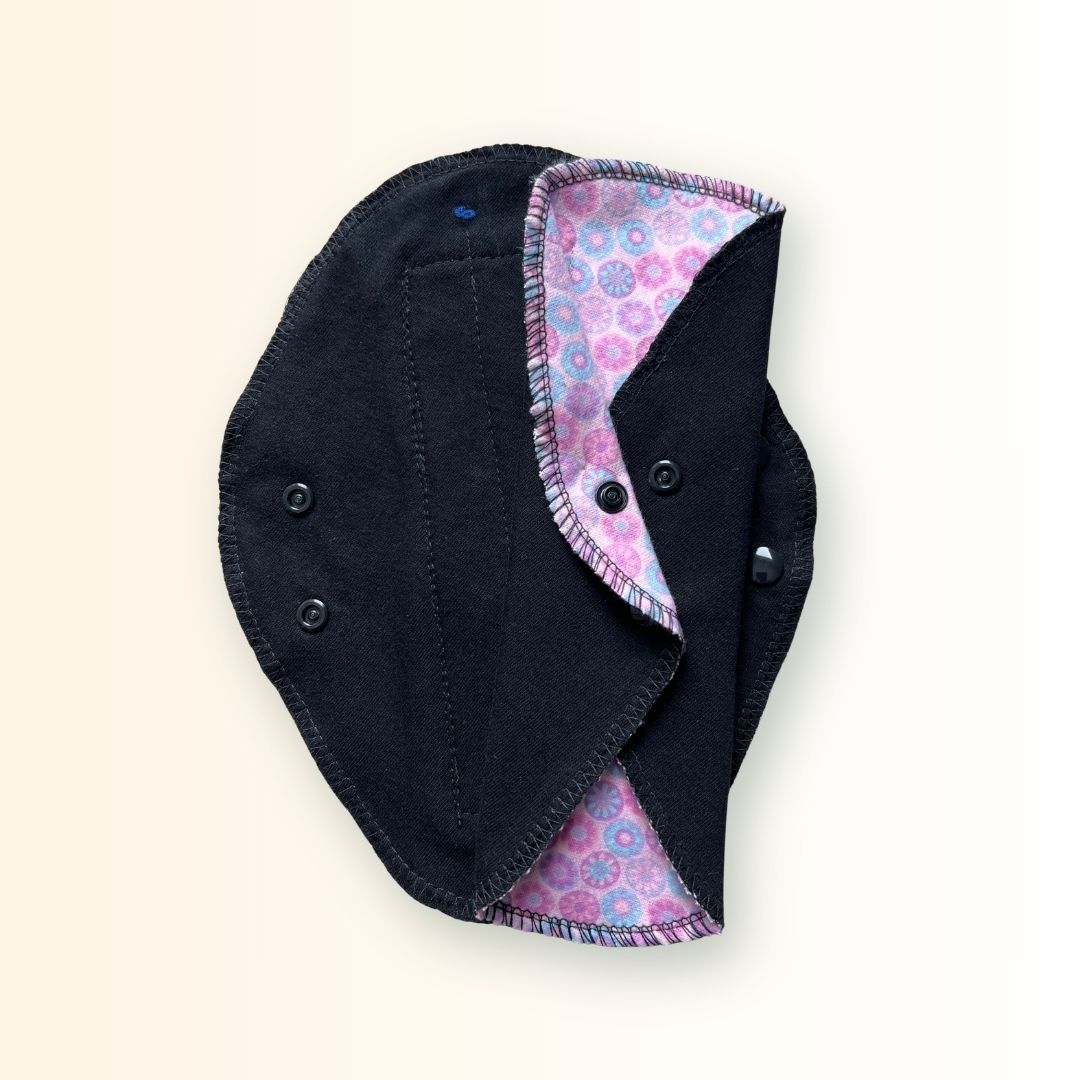 Pink mosaic reusable day pad shown open beside a folded pad with black absorbent fabric.