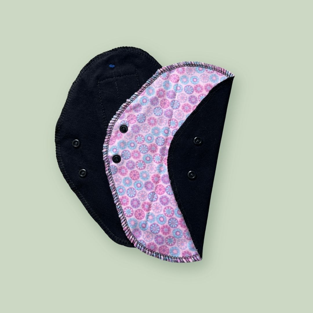 Pink patterned reusable cloth pad with black absorbent fabric and snap wings.