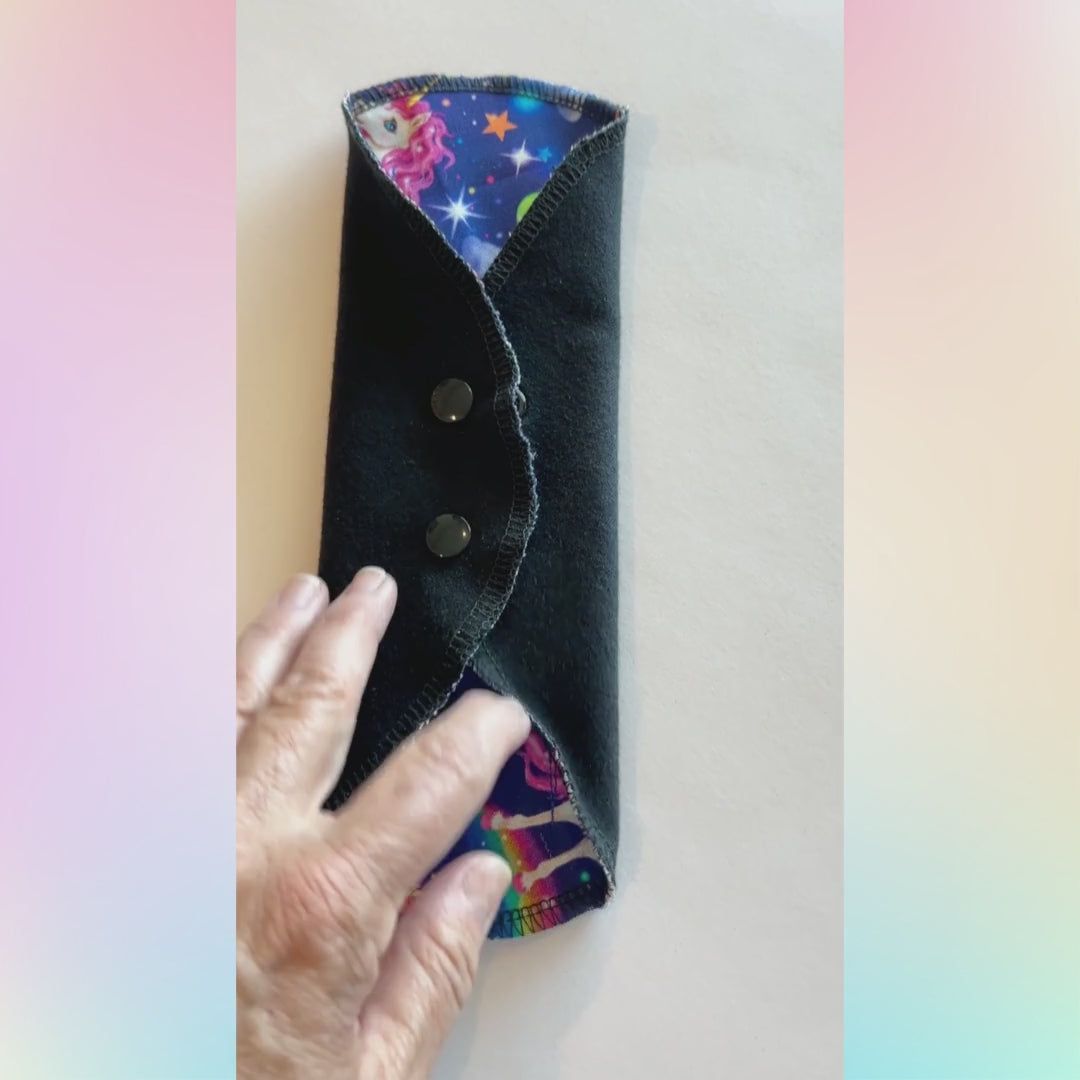 Video showing the Unicorn Galaxy Reusable Period Pad from Hume’s Period Care with rainbow unicorn print, black cotton absorbent side, snap wings, and washable cloth pad design.

