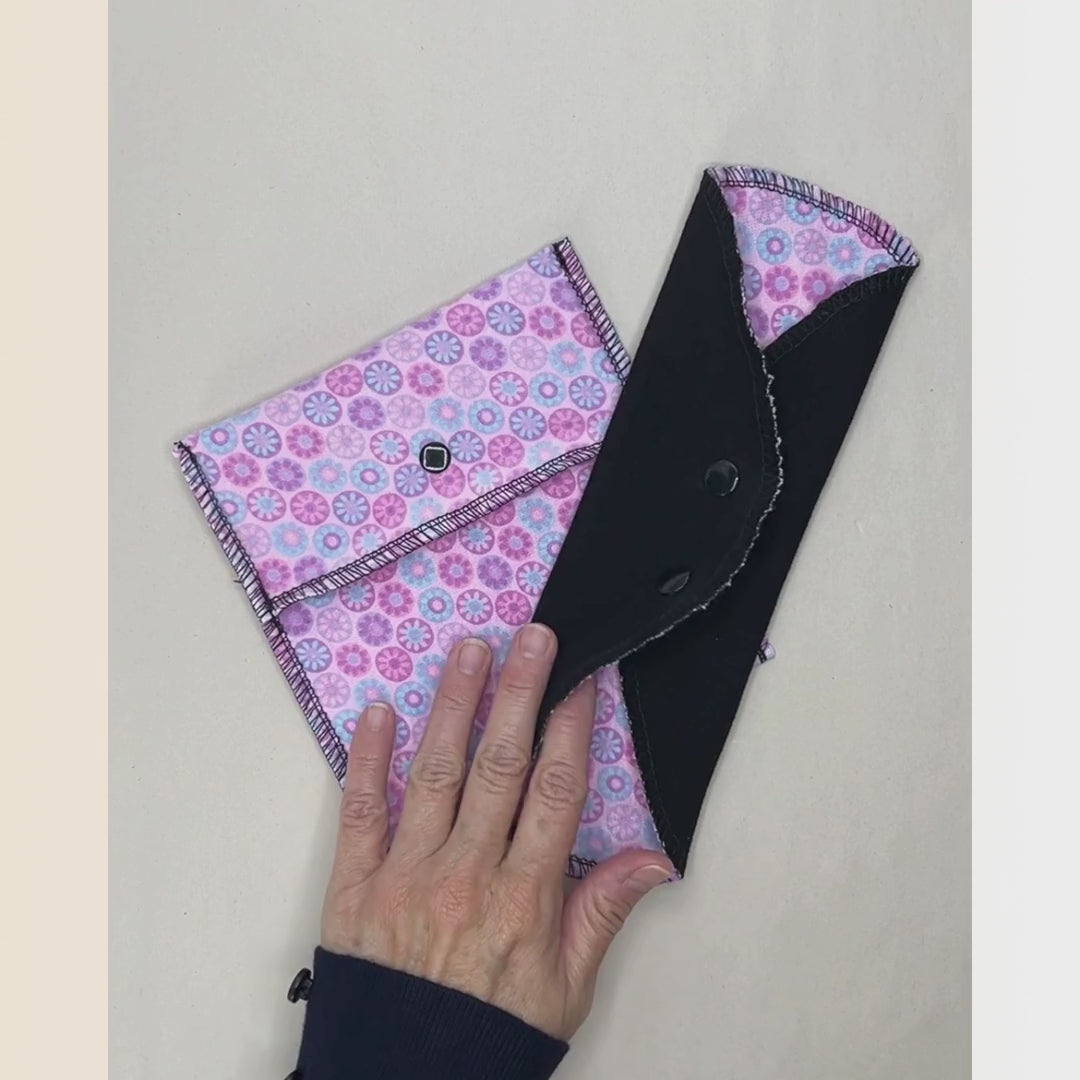 Pink mosaic reusable cloth day pad demonstration showing the print, black absorbent side, snap wings, folding, and compact storage.