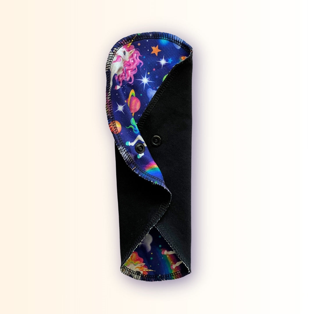 Unicorn print reusable period pad standing folded with black absorbent side and colorful rainbow galaxy fabric from Hume’s Period Care.