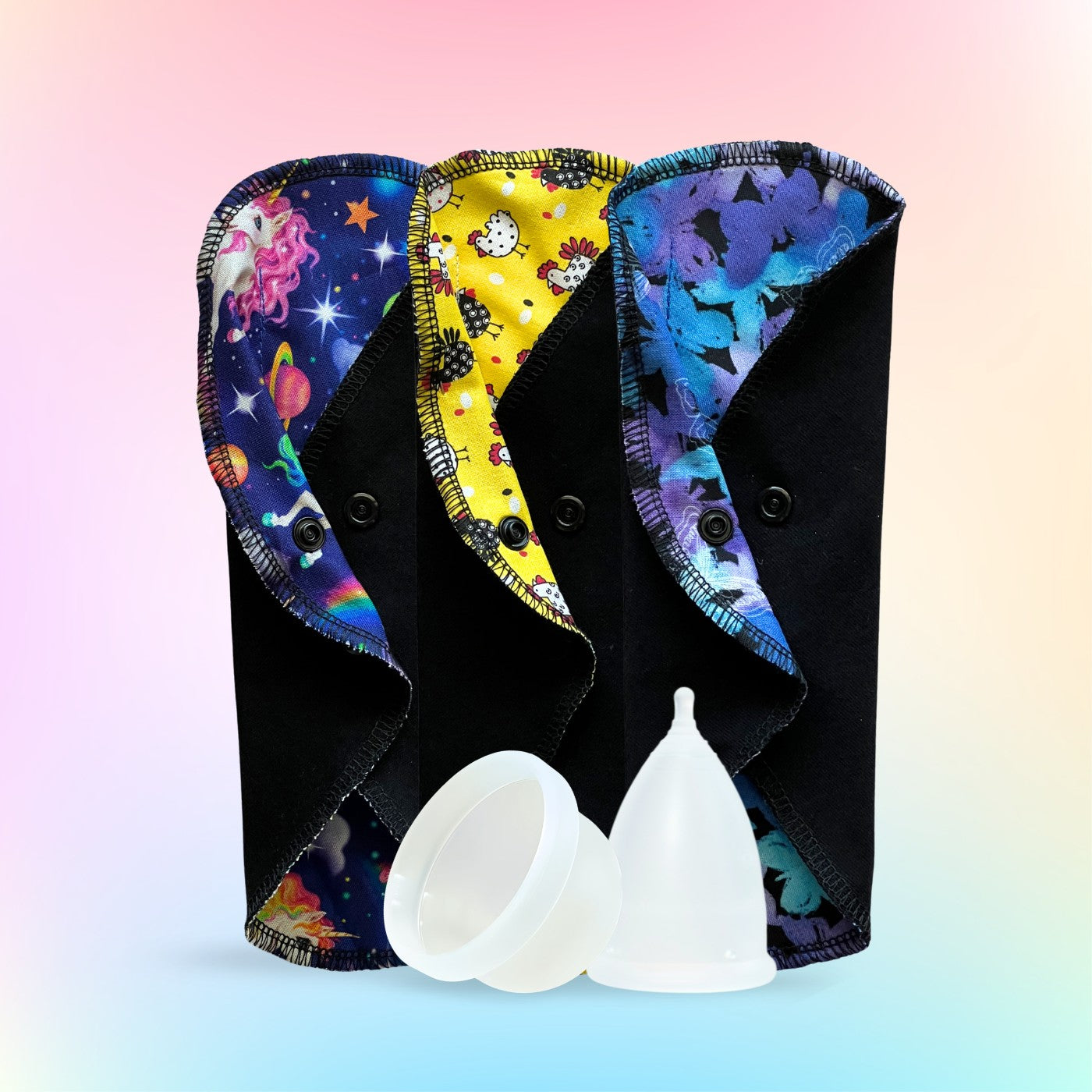 Pride Month-inspired colorful reusable period pads with unicorn, yellow chicken, and blue butterfly prints shown with a menstrual cup and disc from Hume’s Period Care.