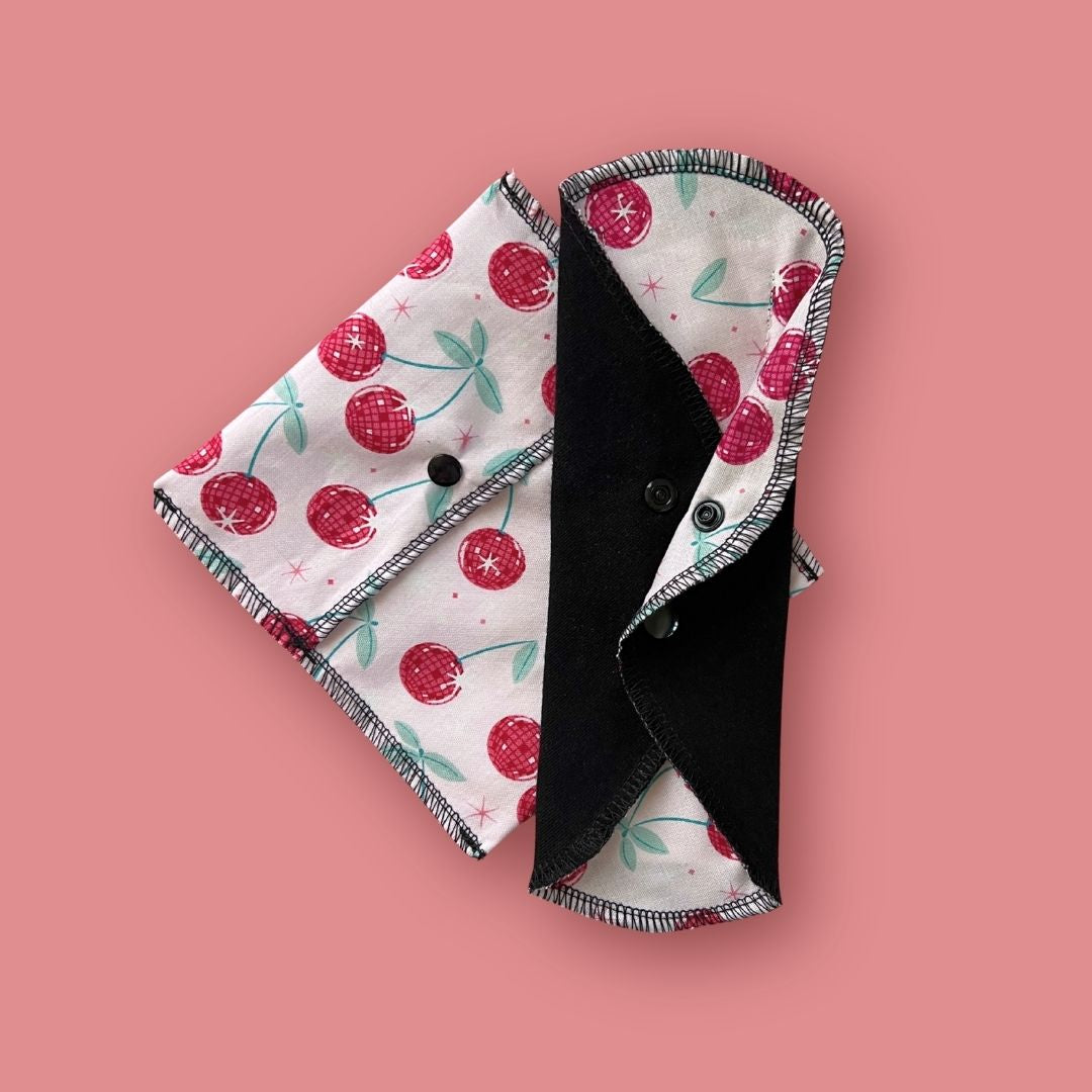 Reusable cloth pad with matching cherry print carry pouch on pink background