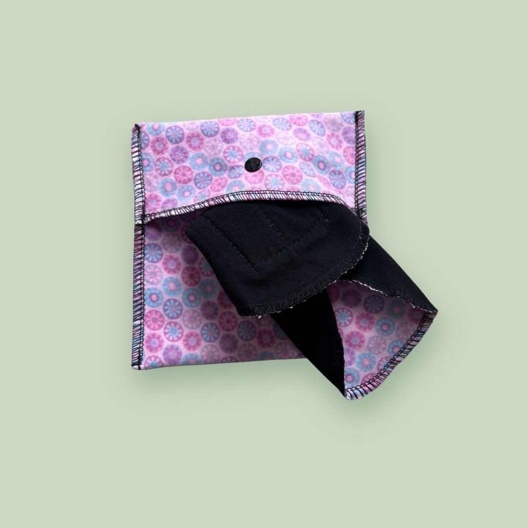 Pink reusable travel wrapper open with folded cloth period pads stored inside.