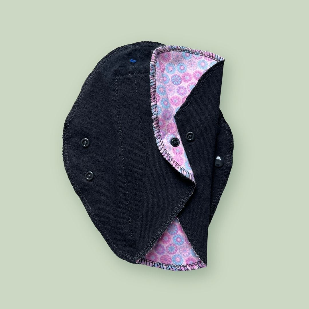 Black absorbent side of a reusable cloth pad showing the wings and snap closure.