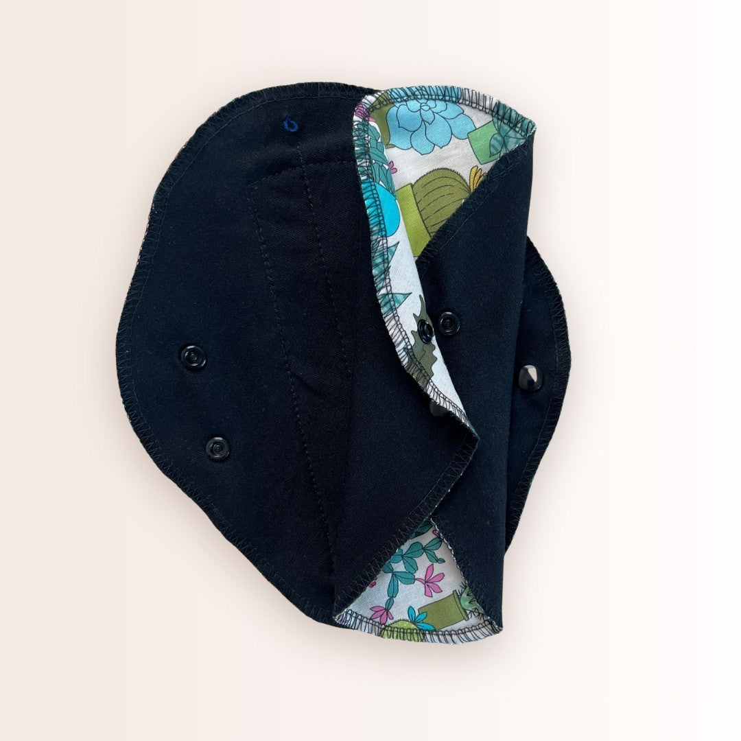 Washable day pad in a cactus bloom print with black cotton absorbent side.