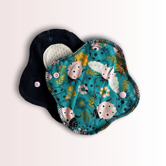 Reusable cloth pad showing front print and black back side with snap closure – eco-friendly, washable design