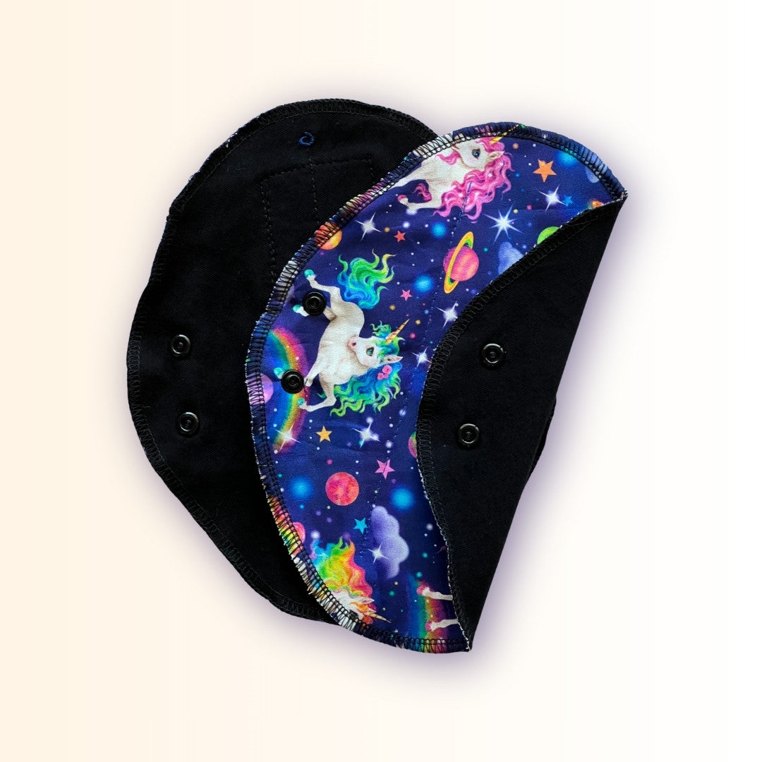 Unicorn reusable period pad shown open and folded, with rainbow galaxy print, black cotton side, and snap closure from Hume’s Period Care.