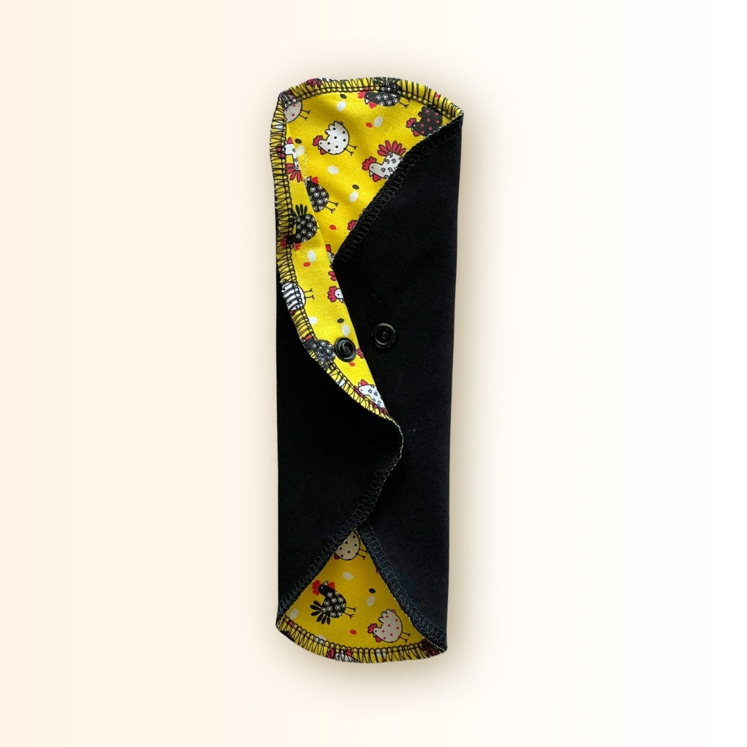 Yellow Chicken Reusable Period Pad standing folded with black cotton absorbent side, snap closure, and bright yellow chicken print from Hume’s Period Care.