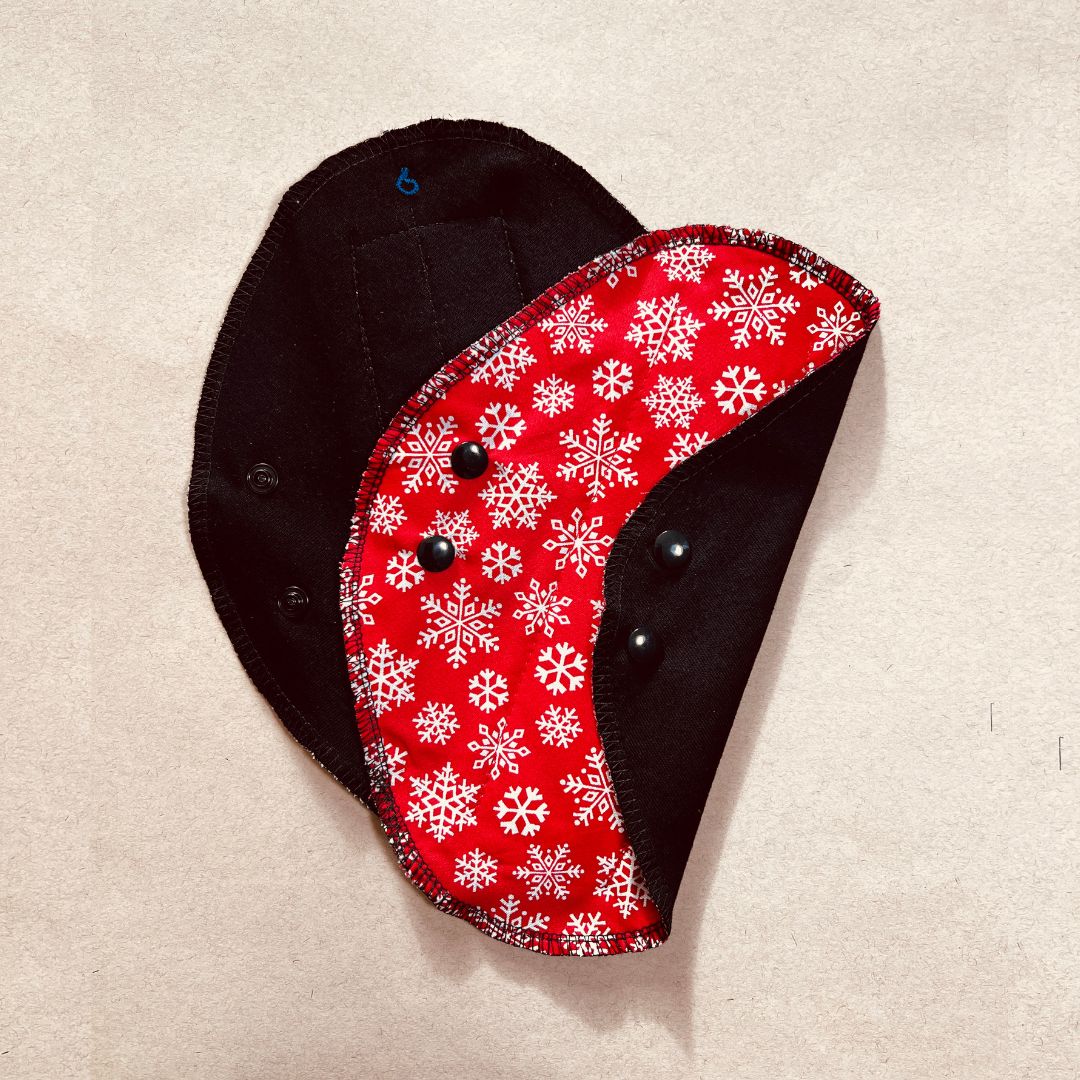 Black reusable menstrual pad with Christmas print — organic cotton core, holiday edition folded on one half
